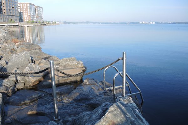 Massunlasten uimapaikka: vasemmalla kivinen ranta ja metalliset veteen johtavat tikkaat. Oikealla sinistä vettä. Taka-alalla vasemmalla Tampellan punatiilisiä kerrostaloja.