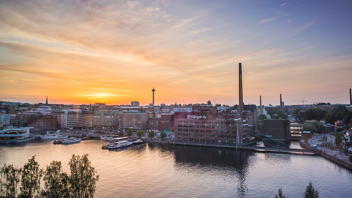 Auringonlasku Laukontorin yllä: taustalla näkyy Tampereen punaisia tiilirakennuksia, korkea savupiippu ja Näsinneula. Etualalla sininen ja oranssi taivas heijastuu suvannon vedestä.