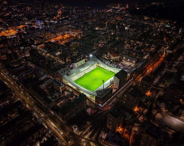Valaistu stadion kuvattu pimeältä taivaalta, kaupungin valoja.